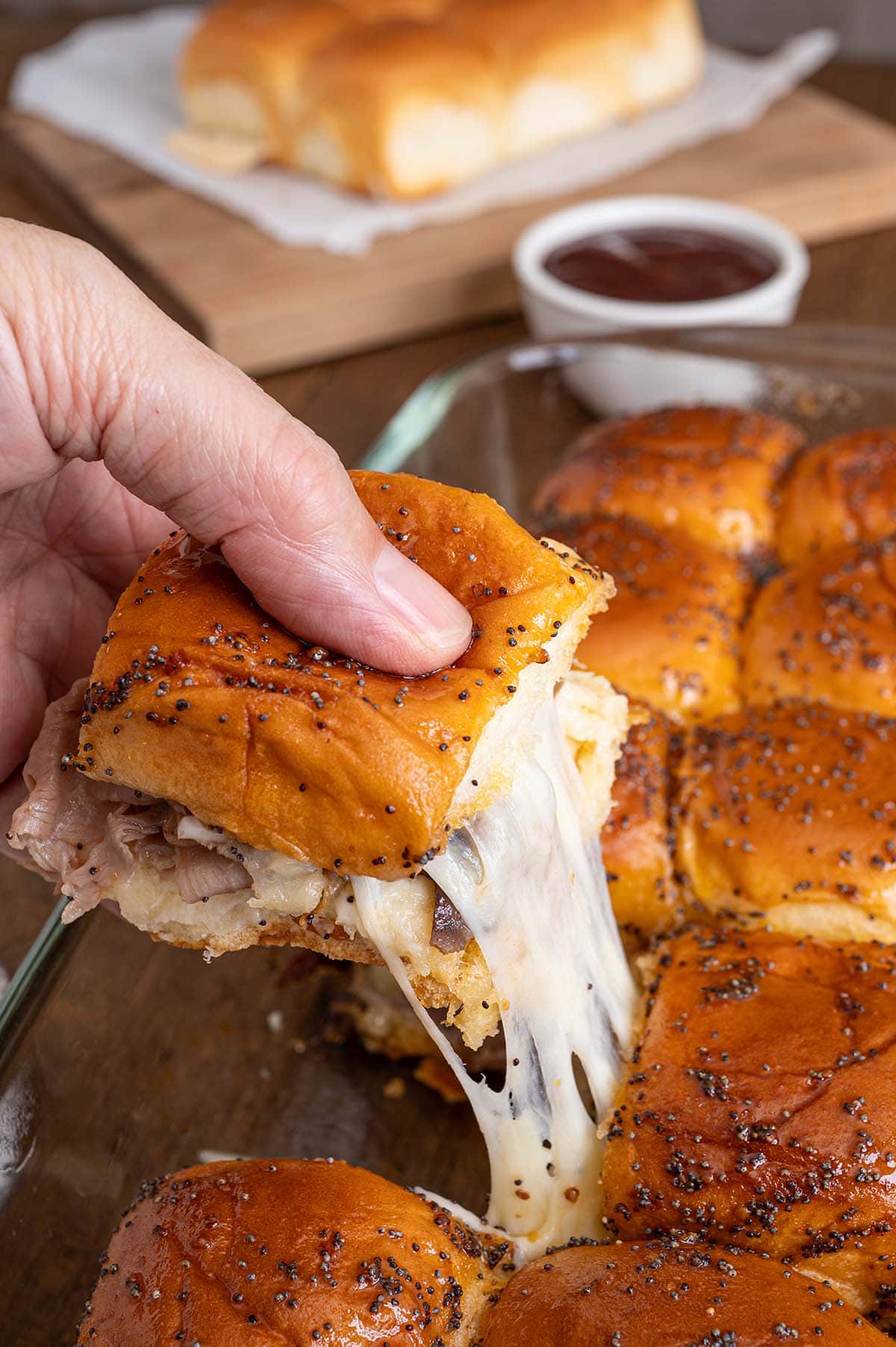 Hand lifts a roast beef slider from the dish. Melted cheese stretches between bun halves.