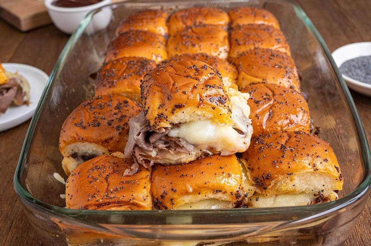 Roast beef sliders with melted cheese on sesame buns in a glass dish.