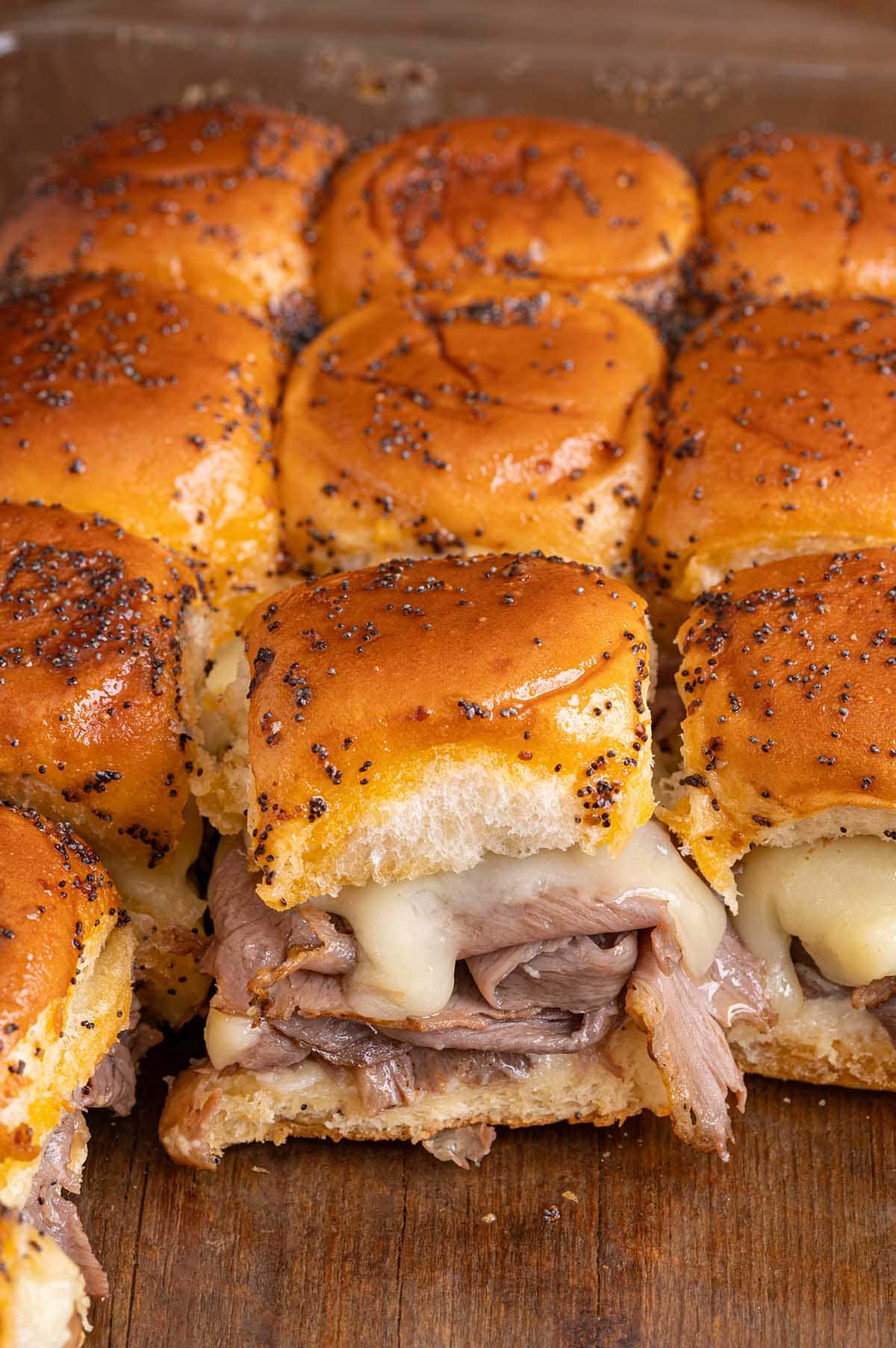 Tray of roast beef sliders with melted cheese on sesame buns.