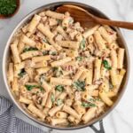 Creamy Italian sausage pasta in a skillet with spinach and sun-dried tomatoes.