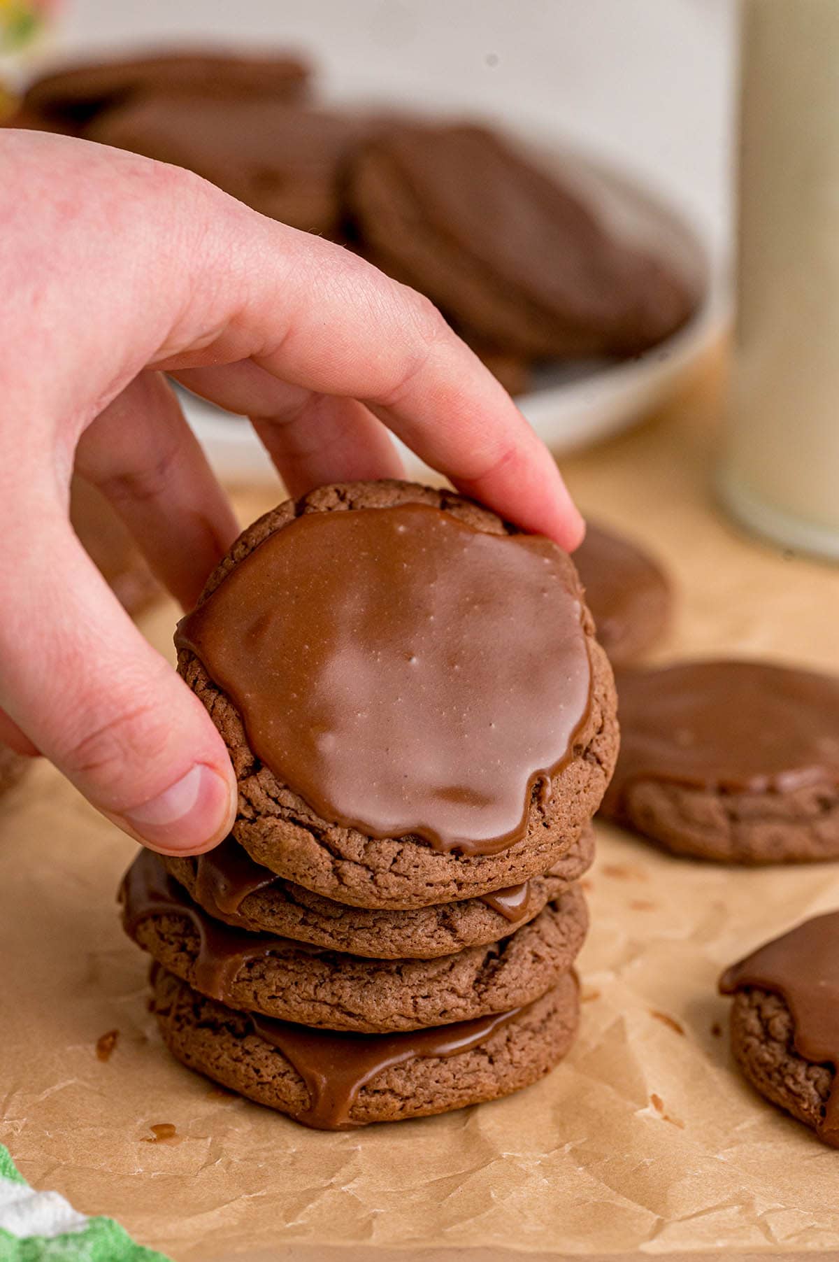 Stack of four Texas sheet cake cookies topped with shiny chocolate icing sits next to a glass of milk.