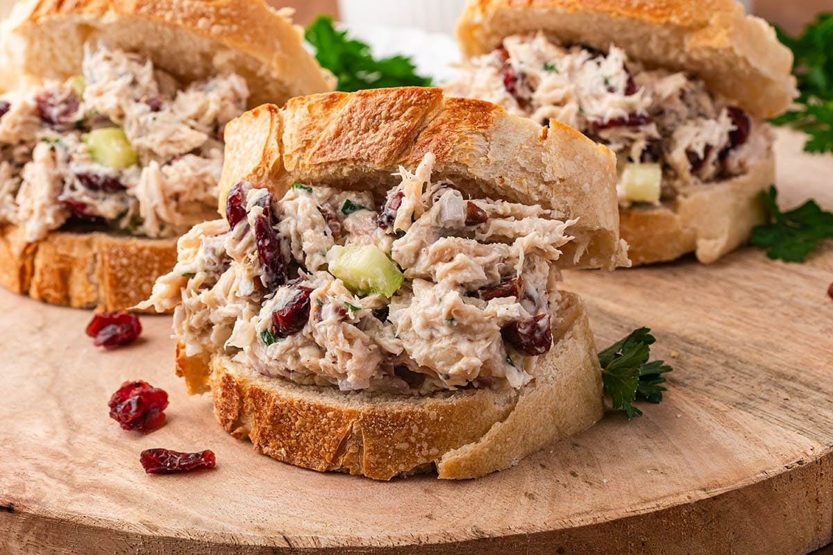 Cranberry chicken salad fills golden buns, topped with fresh parsley on wood.