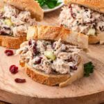 Open-faced cranberry chicken salad sandwiches on a wooden board with fresh parsley.