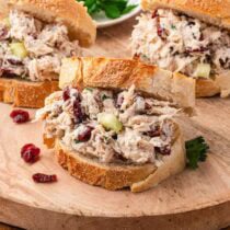 Open-faced cranberry chicken salad sandwiches on a wooden board with fresh parsley.