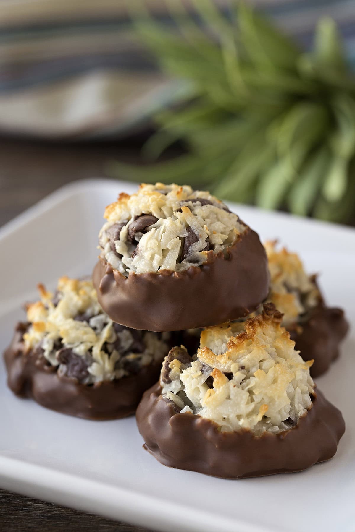 Stack of chocolate-dipped chocolate chip macaroons on a white square plate.