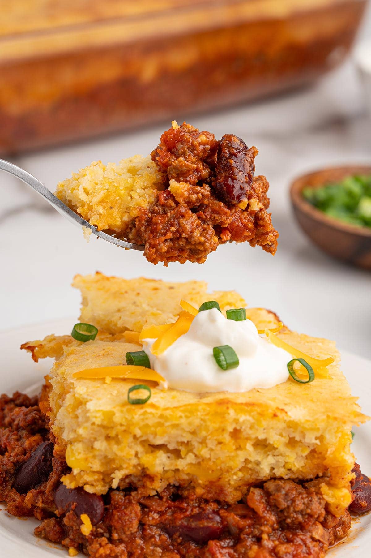Slice of chili cornbread casserole on a plate, topped with sour cream and green onions.