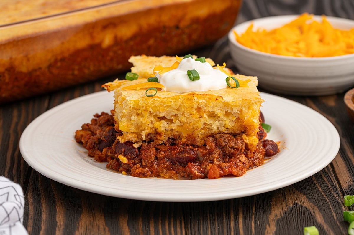 Slice of chili cornbread casserole on a white plate, topped with sour cream and green onions.