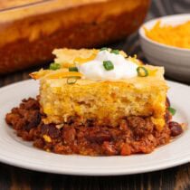 Close-up view of layered chili cornbread casserole; sour cream and onions add fresh contrast.