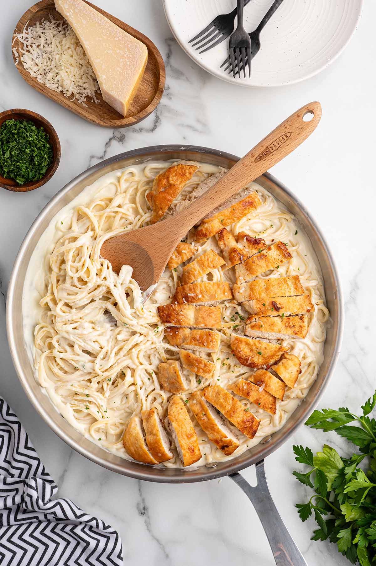Pan of creamy chicken pasta with golden breaded chicken pieces and fettuccine in white sauce, wooden spoon inside.