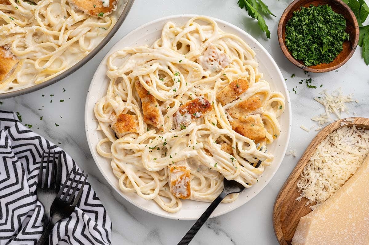 Plate of creamy chicken pasta topped with golden chicken pieces and fresh parsley.