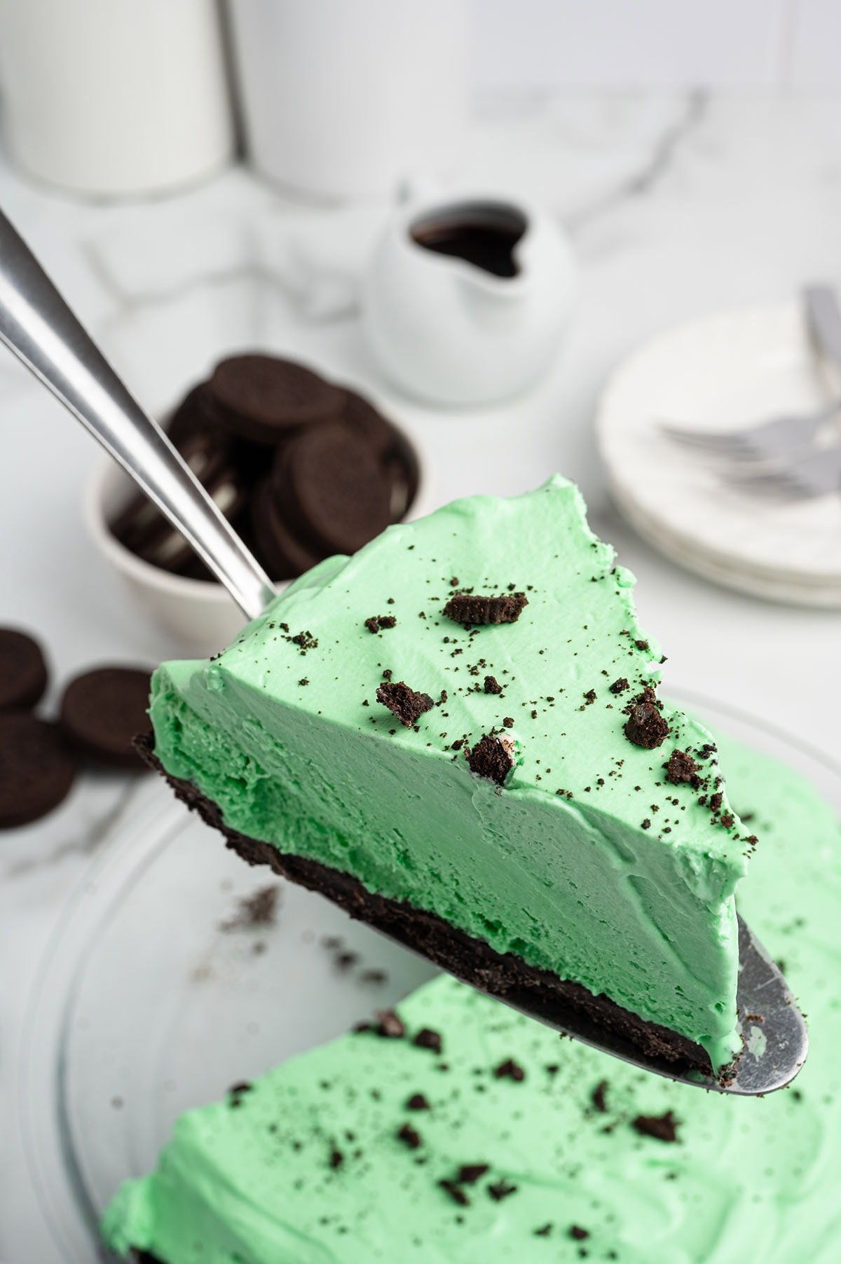 Slice of creamy green Grasshopper pie topped with Oreo crumbs on a silver server.