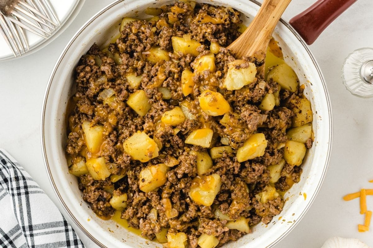 Hamburger hash cooks in a white pot; chunks of potato mix with browned beef and yellow gravy.