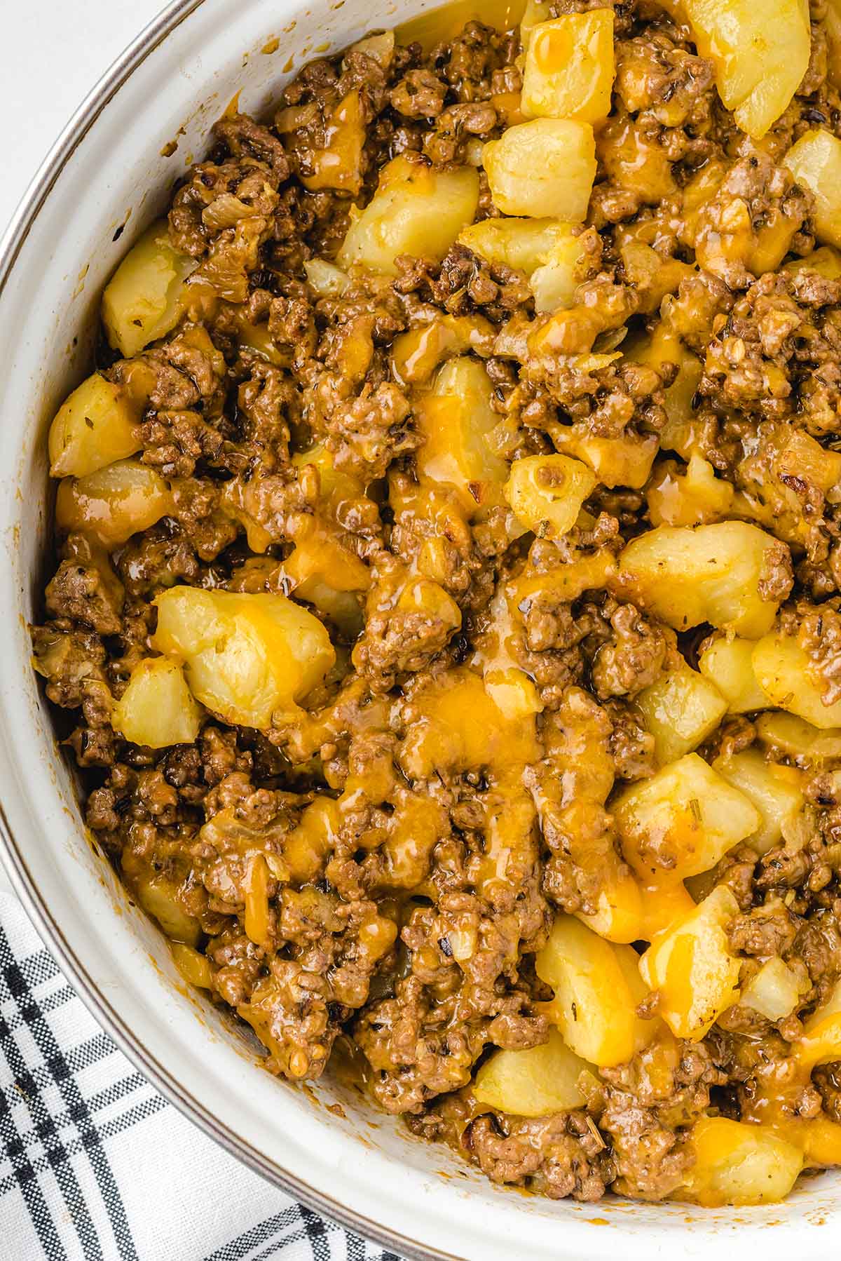 Hamburger hash in a white bowl with diced potatoes, ground beef, and melted cheese.