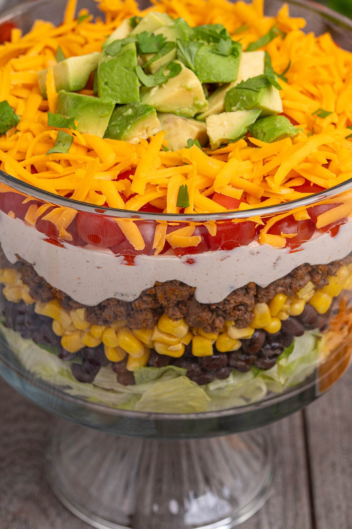 Closeup of a trifle-style layered taco salad with colorful layers including beef, veggies, and cheese on top.