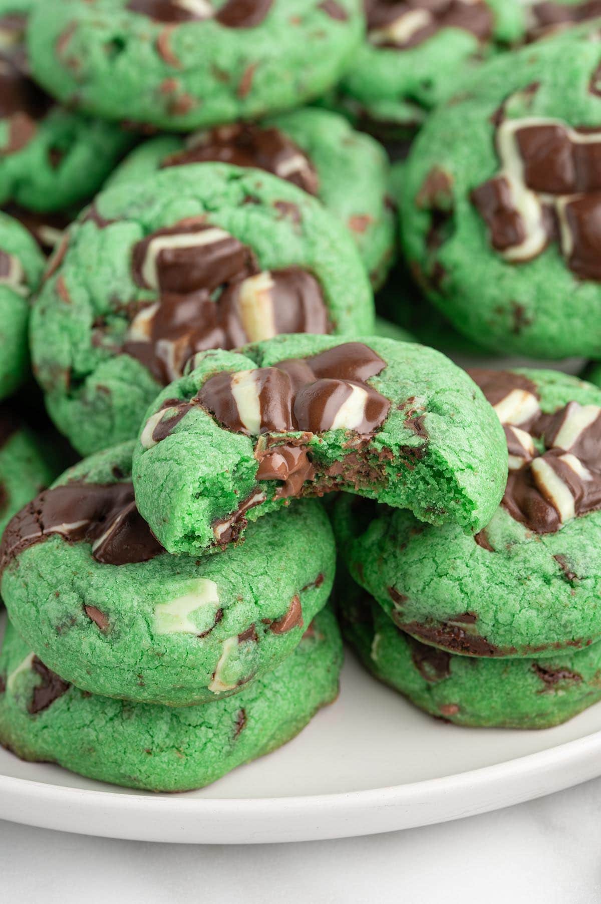 Stack of green mint chocolate chip cookies with white and dark chocolate chunks on a white plate.