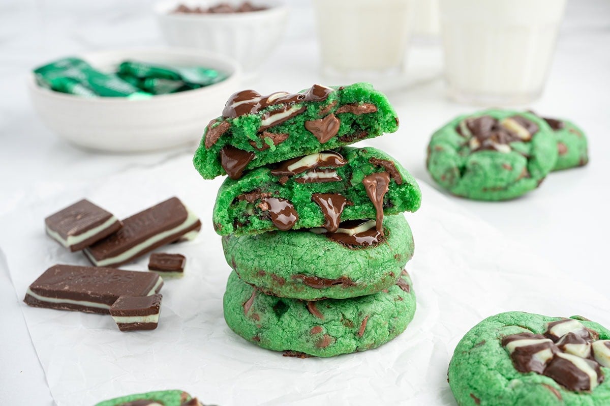 Stack of green mint chocolate chip cookies with milk glasses nearby.