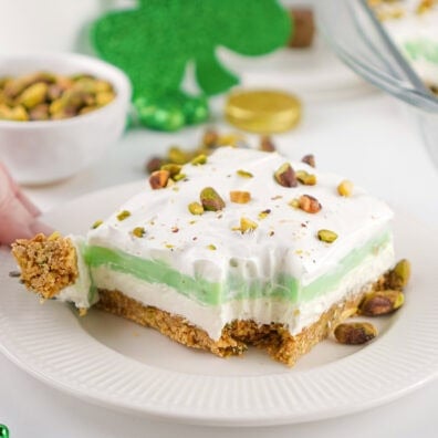 Slice of pistachio pudding dessert with whipped topping, green layer, and pistachios on a white plate.