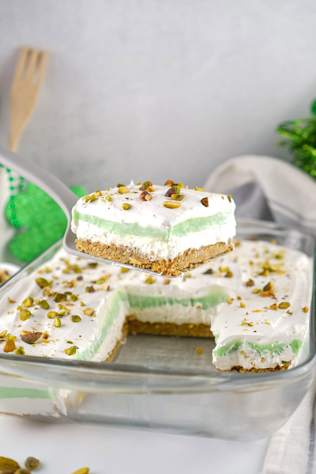 Slice of layered pistachio pudding dessert on a spatula with green cream and pistachios.