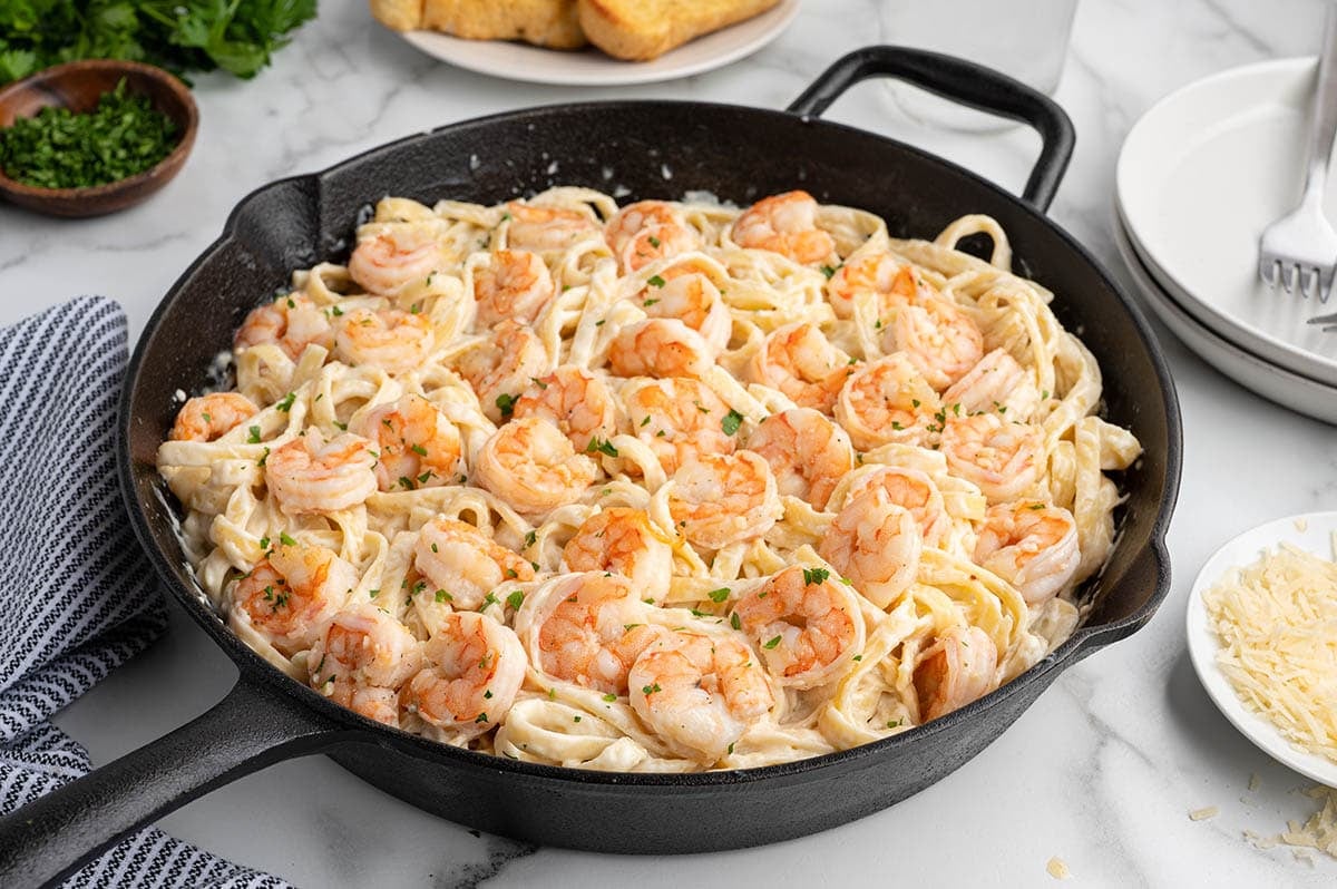 Creamy shrimp alfredo pasta in a black skillet, topped with parsley and shrimp.
