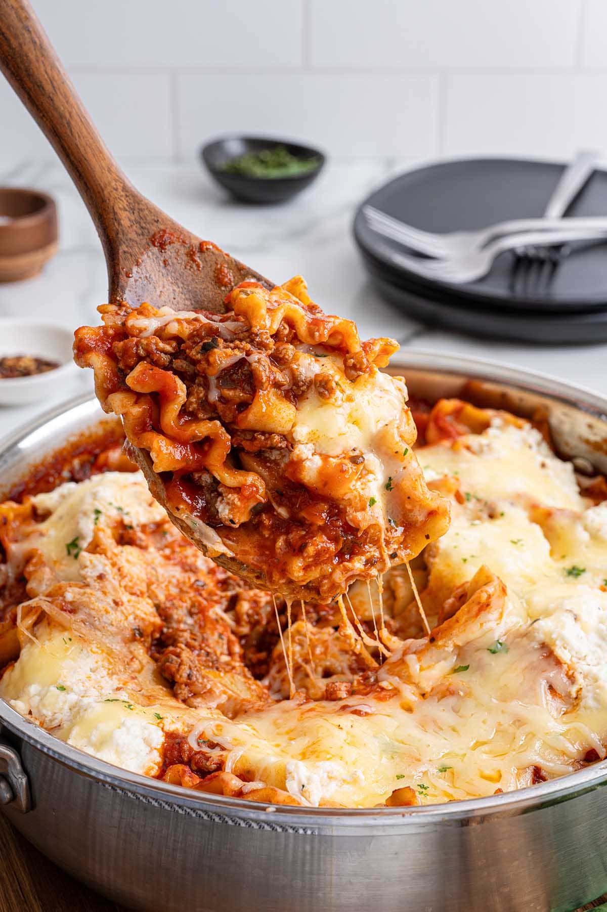 Wooden spoon lifts cheesy skillet lasagna from a stainless steel pan.