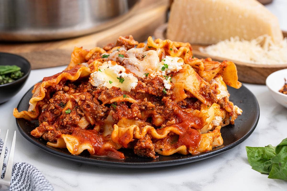 Skillet lasagna on a black plate with red meat sauce and white cheese crumbles.