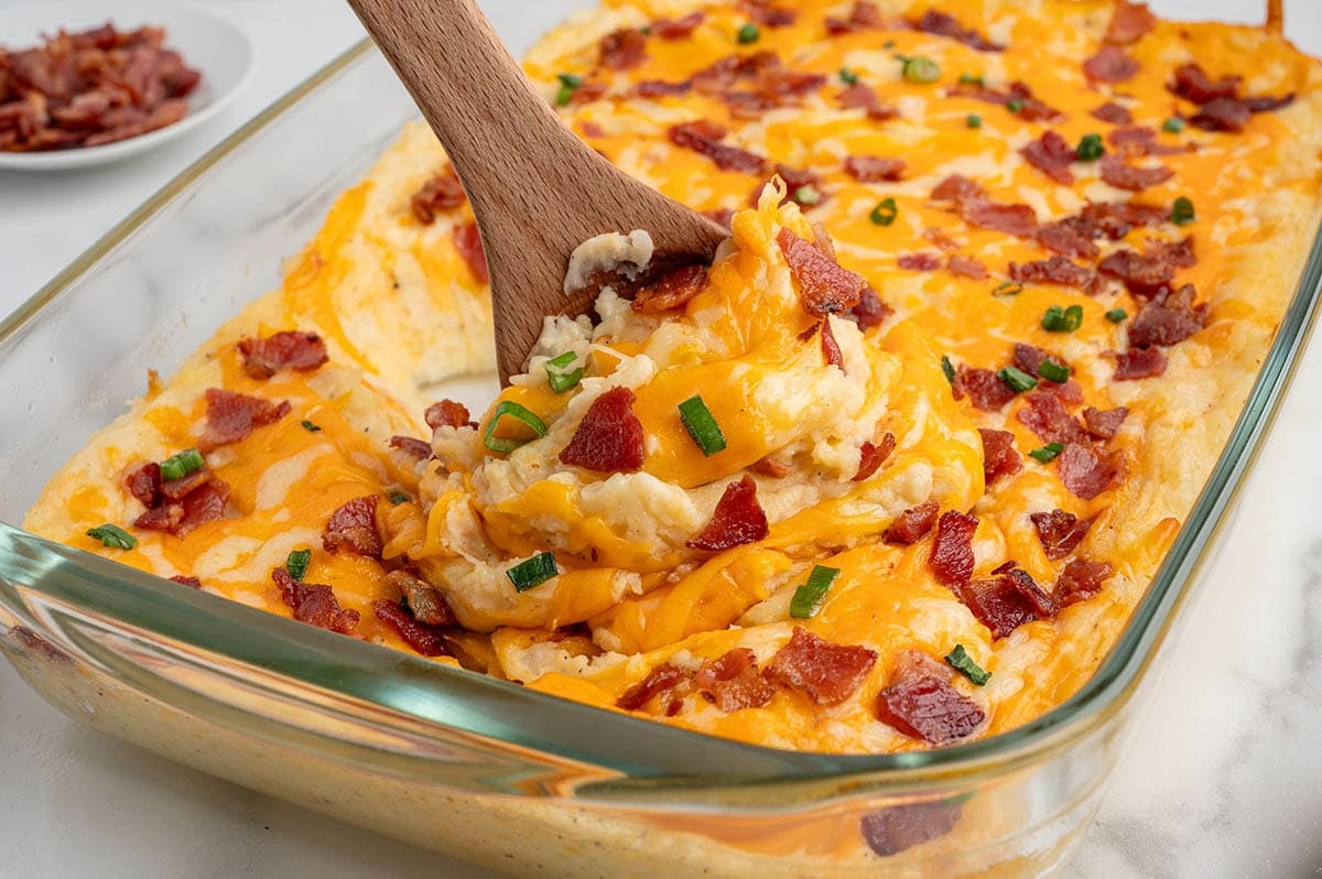 Twice baked potato casserole topped with melted cheese, bacon bits, and green onions in a glass dish.