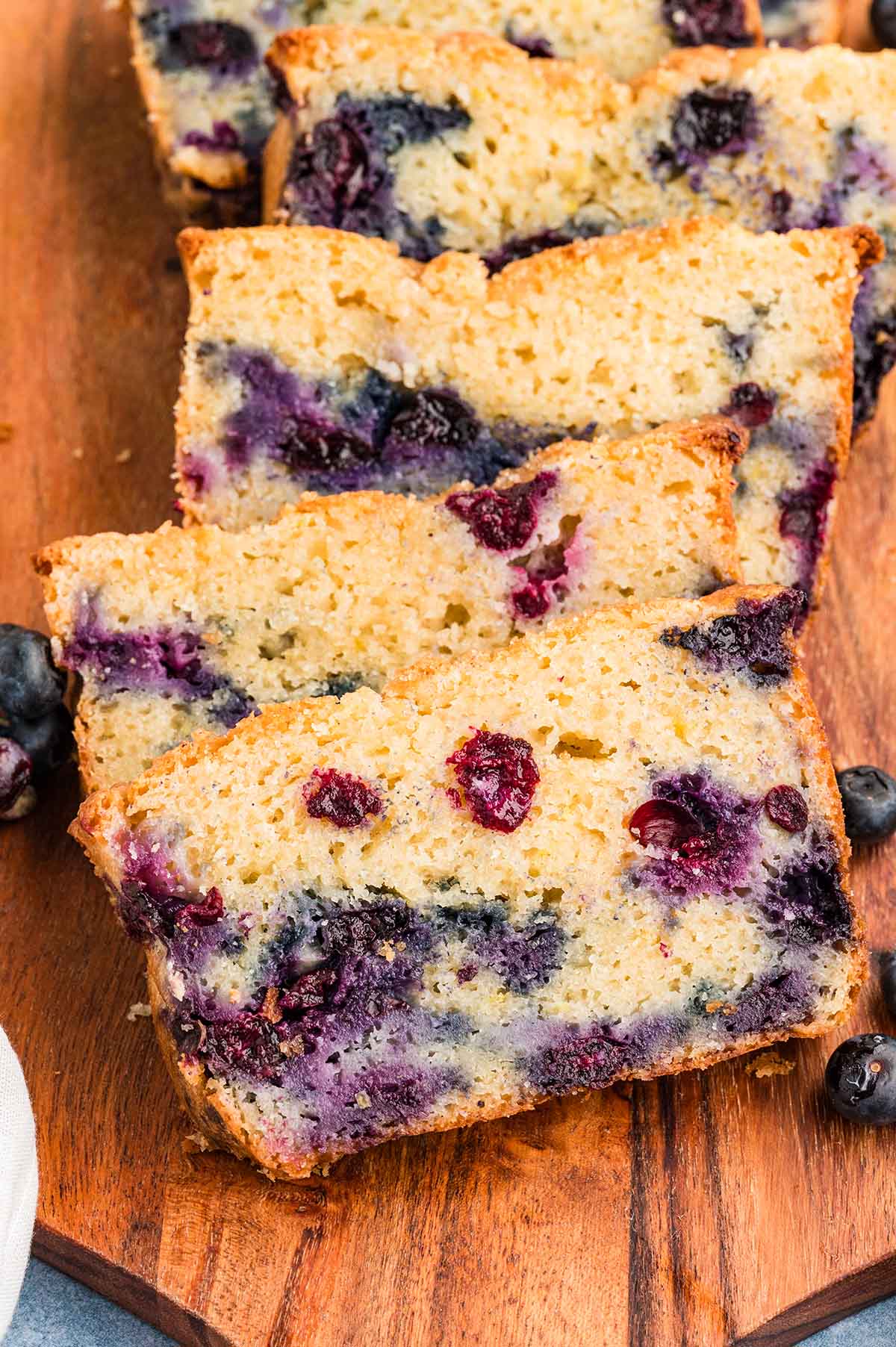 Close-up of sliced blueberry muffin bread showing soft, fluffy texture with juicy blueberries throughout on a wooden board.