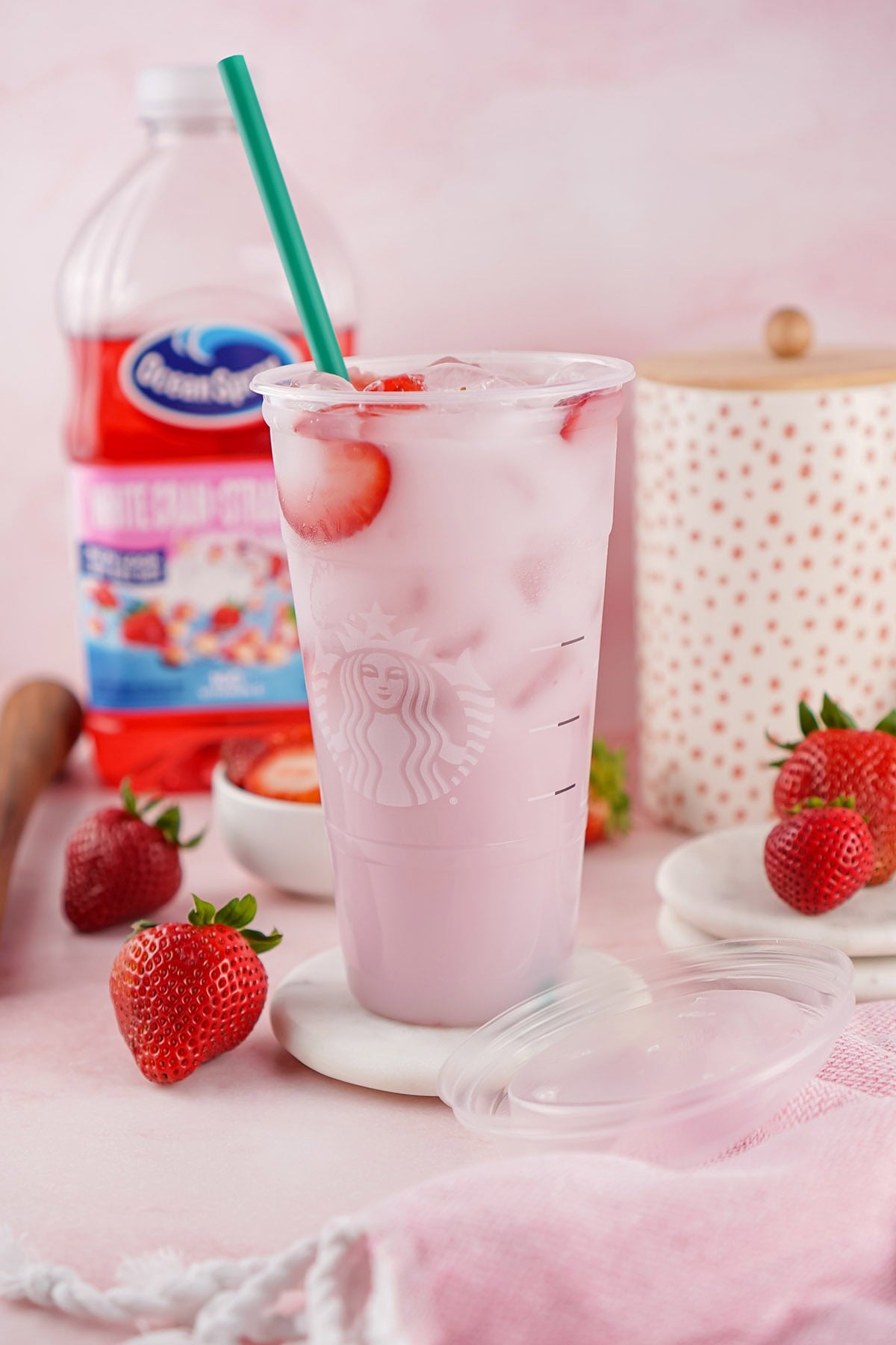 Starbucks Pink Drink in a clear cup with green straw and fresh strawberry slices on top.