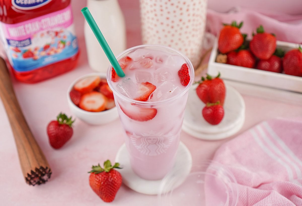 Starbucks Pink Drink in a clear cup with ice, strawberry slices, and green straw.