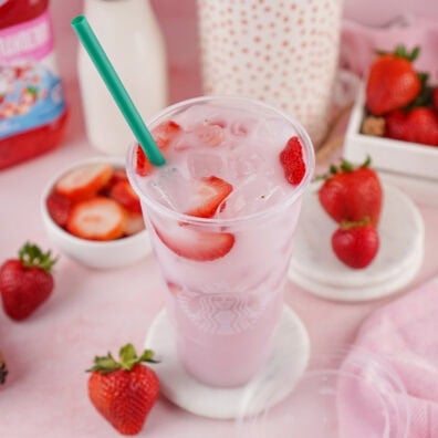 Copycat Starbucks Pink Drink with fresh strawberries and a green straw on a pink background.