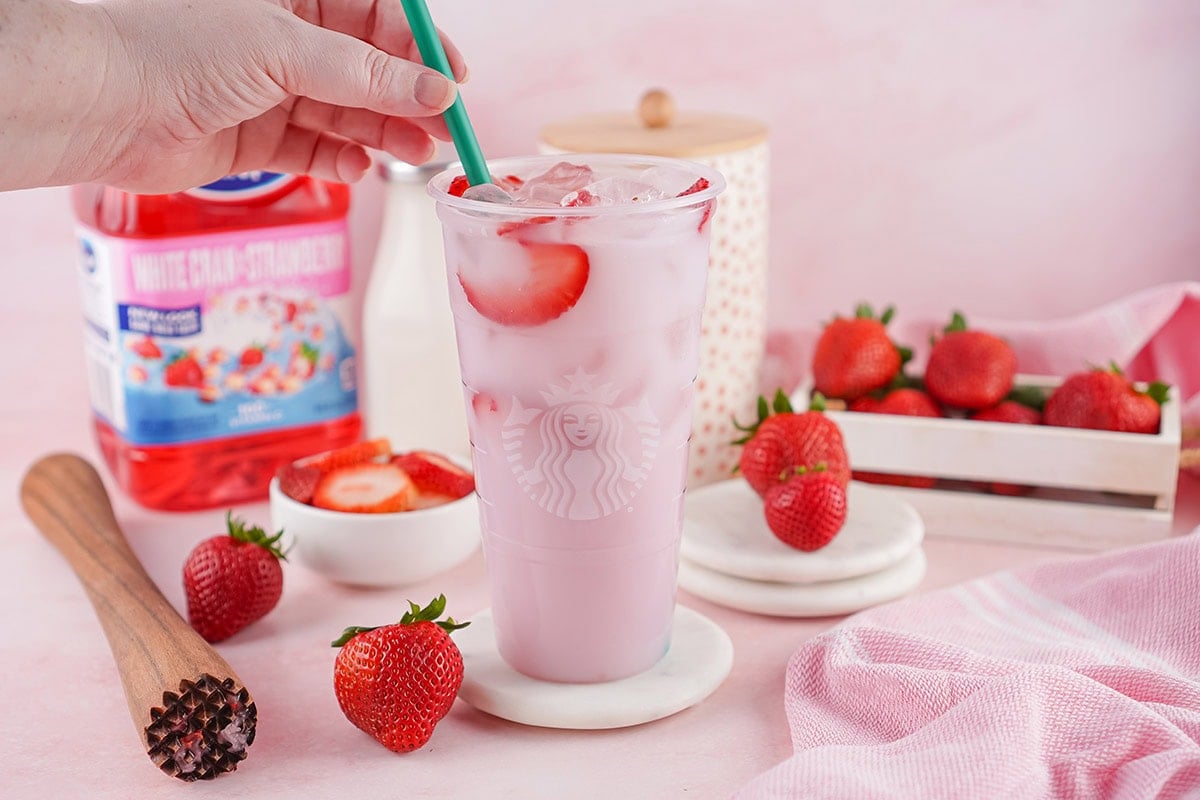 Starbucks Pink Drink in a clear cup with ice and strawberry slices, green straw ready to sip.