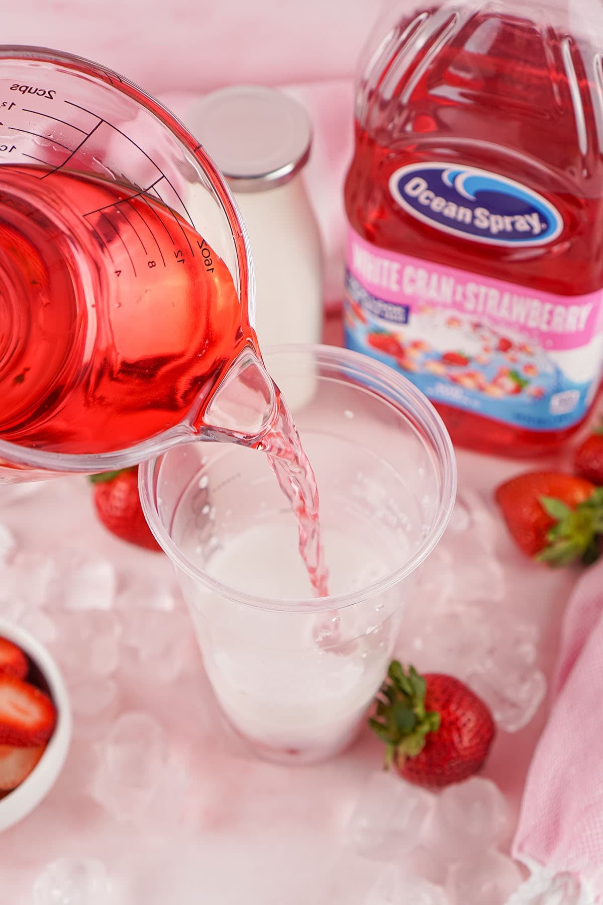 Barista pours pink Ocean Spray cran-strawberry juice into a cup of milk over ice, with fresh strawberries nearby.