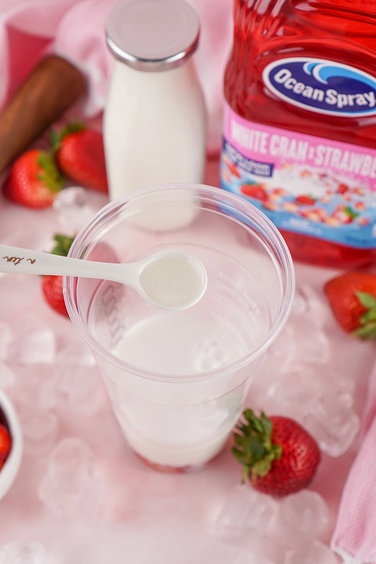 Ocean Spray juice, milk, sliced strawberries, ice, and strawberry powder ready for Starbucks Pink Drink in a cup.