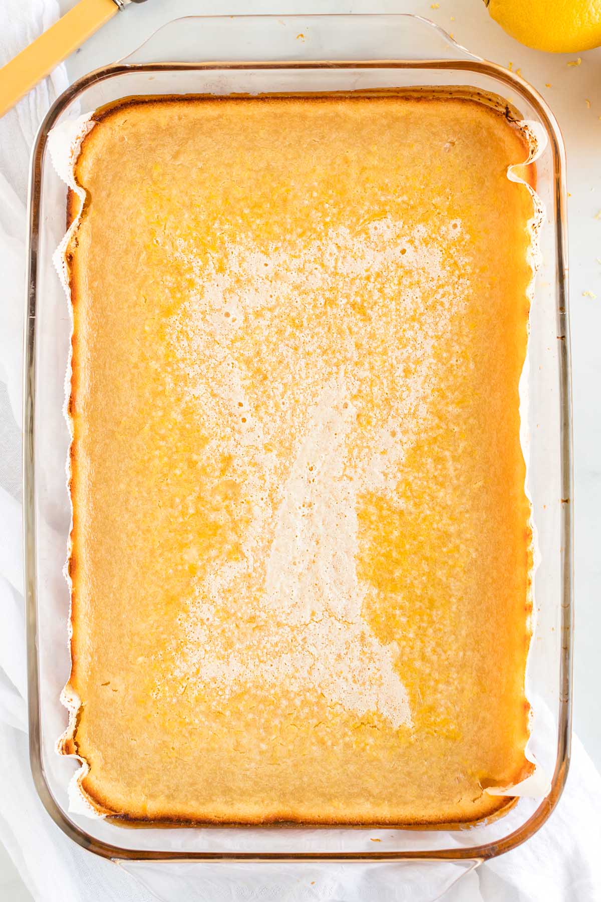 Baked lemon curd filling in a glass pan before dusting with sugar.