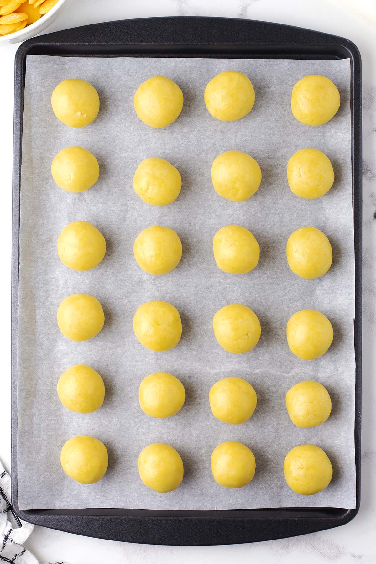 Rows of small yellow lemon cheesecake bites on parchment-lined baking sheet.