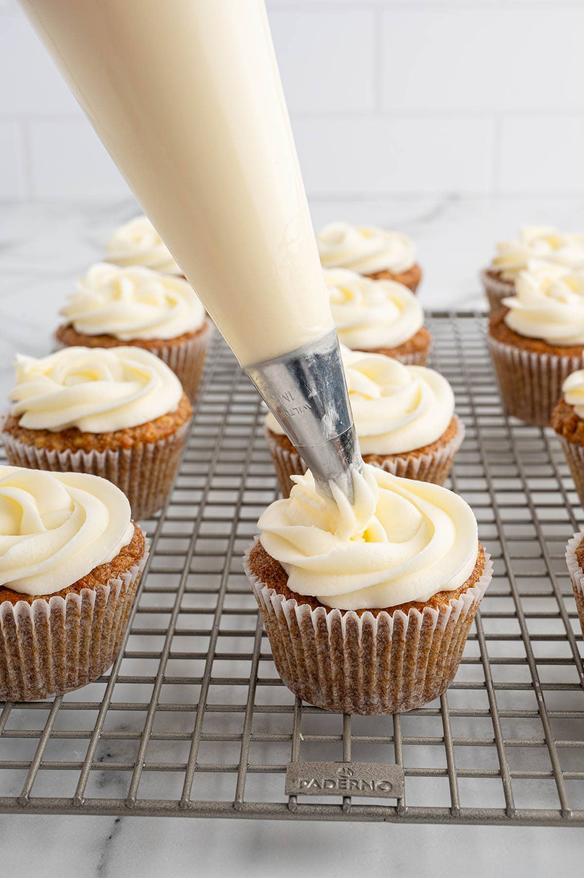 pipe cream cheese frosting on top of carrot cake cupcake. 