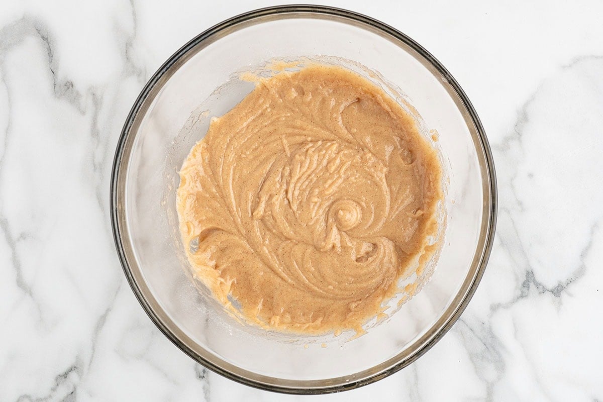 a glass mixing bowl containing smooth, spiced cupcake batter before adding the shredded carrots and pecans.