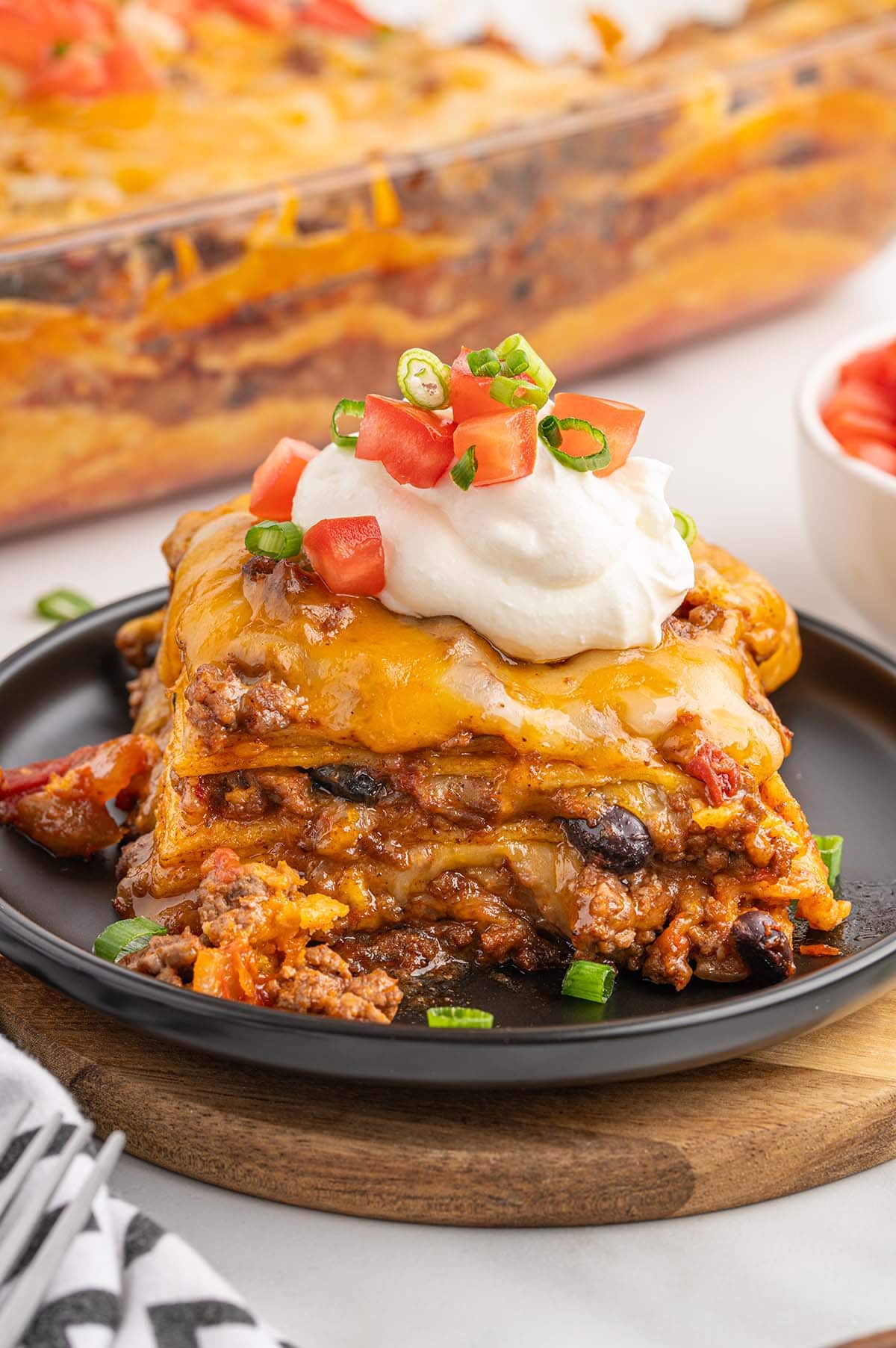 A single square serving of Mexican casserole on a black plate.