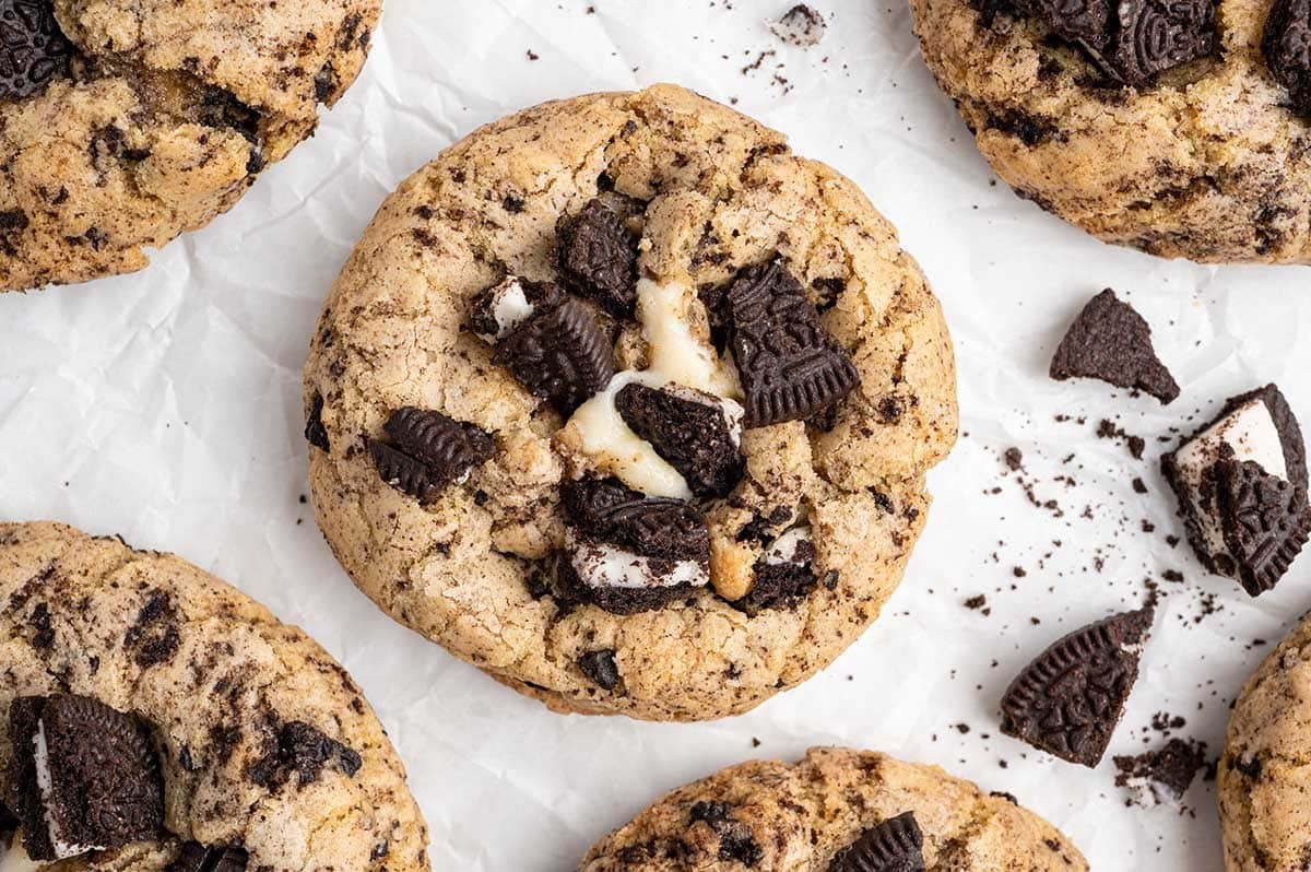 An overhead shot of several Oreo cheesecake cookies on white parchment paper, featuring cracked tops and visible cream cheese centers.