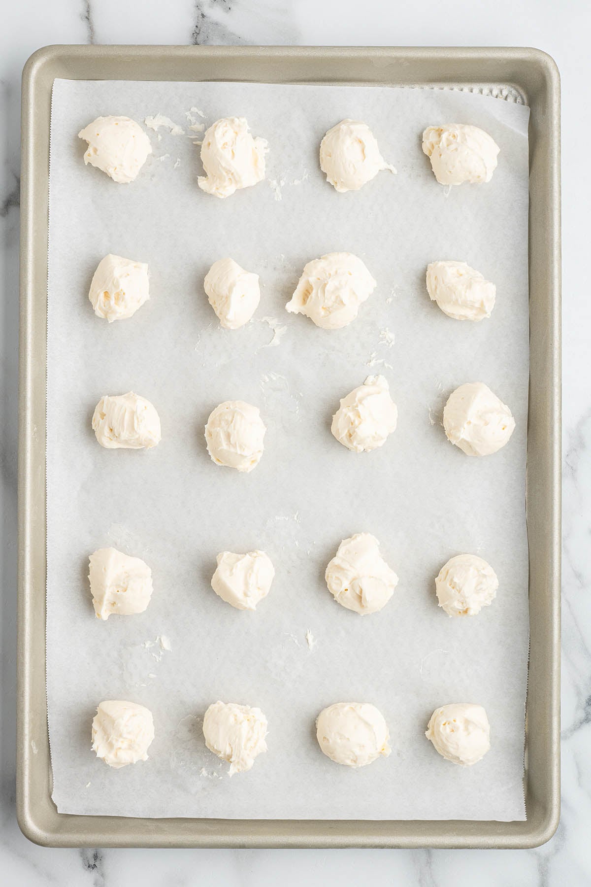 Small scoops of white cream cheese filling spaced out on a parchment lined baking sheet for chilling.