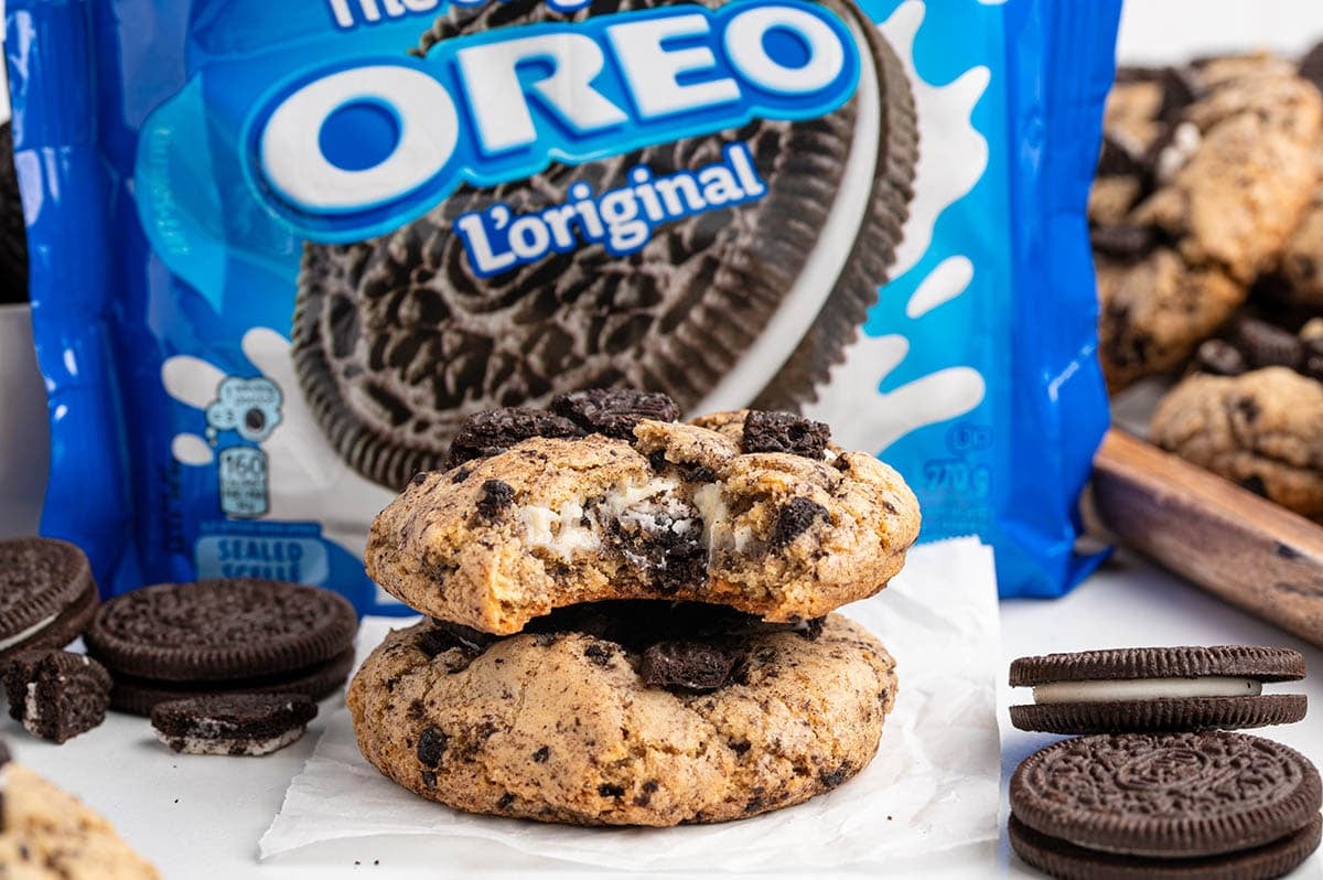 A stack of two thick Oreo cheesecake cookies with a cream cheese center, surrounded by whole and crushed Oreo cookies.