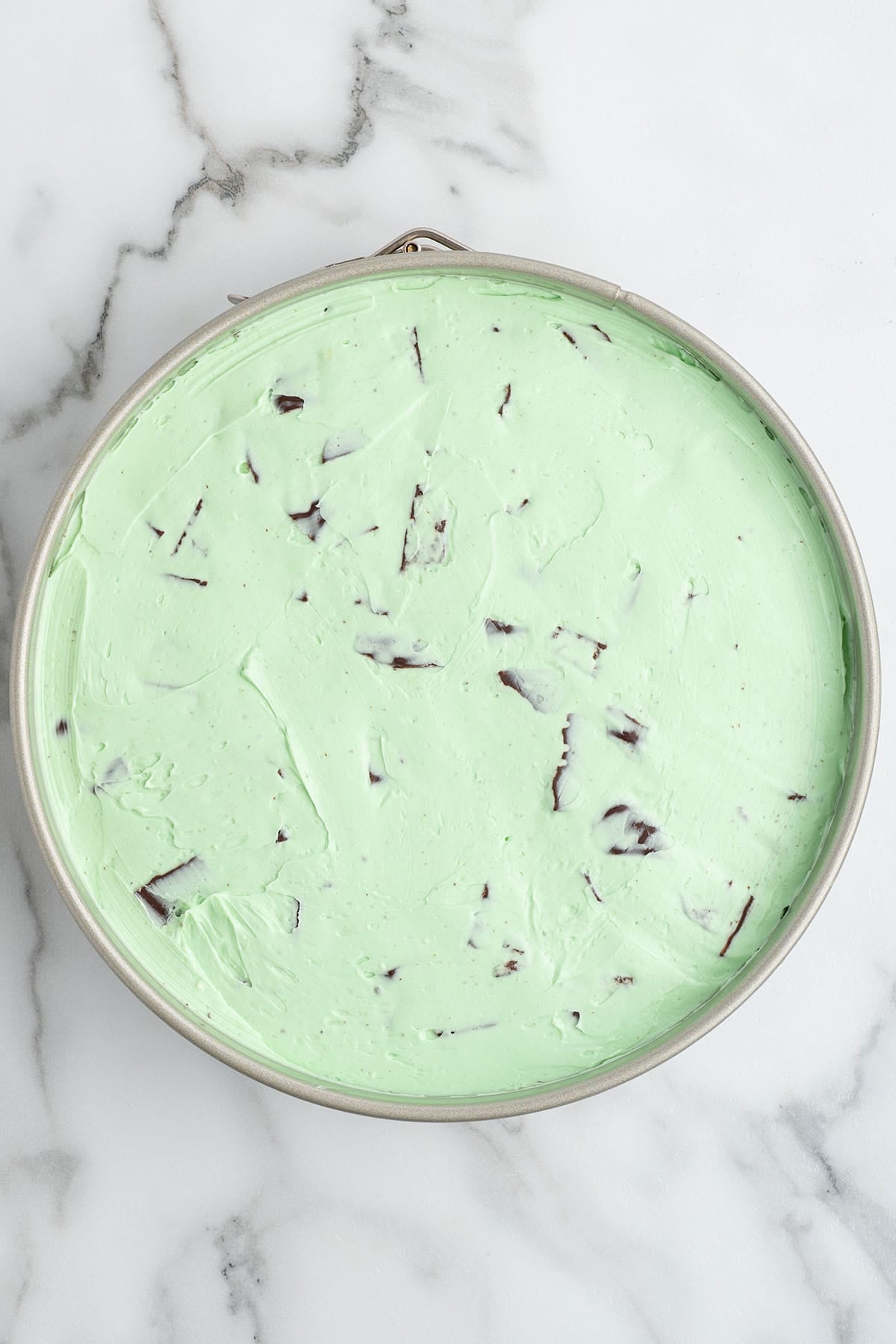 Smooth mint green cheesecake batter mixed with chocolate cookie chunks in a round springform pan.