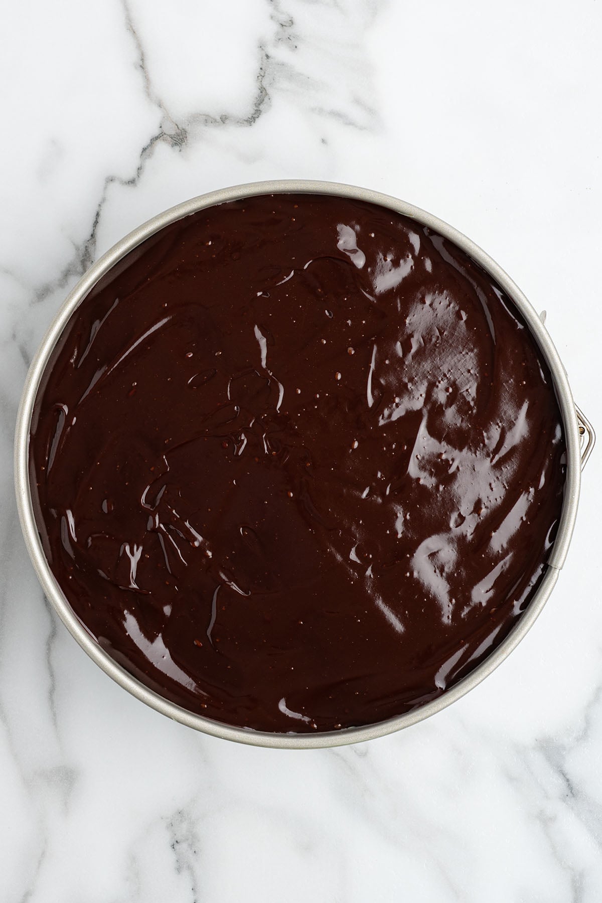 Smooth, glossy dark chocolate ganache spread evenly over the top of a cheesecake in a round springform pan.