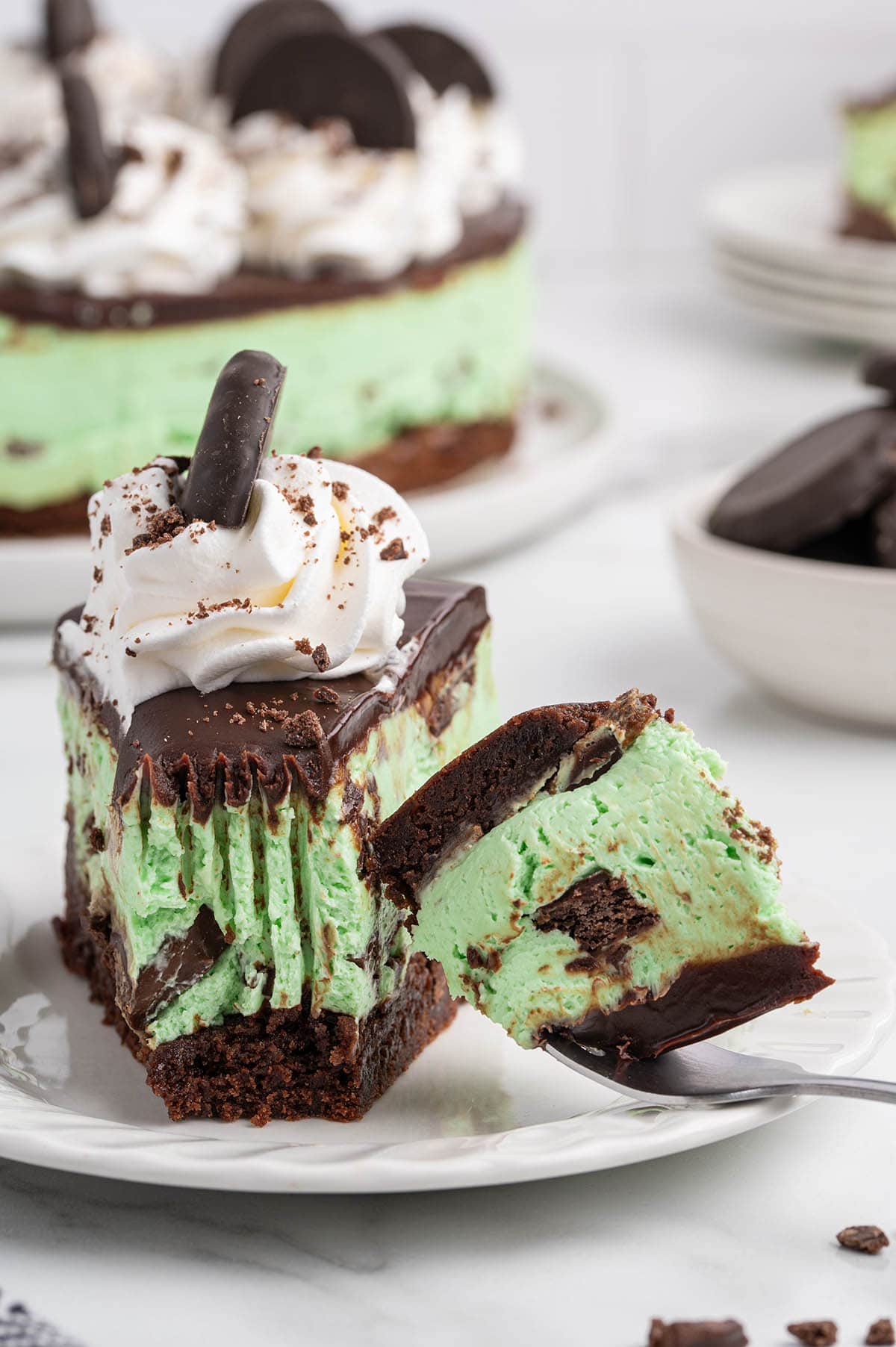 A fork lifting a bite sized piece of mint green cheesecake with a dark chocolate crust and ganache topping.