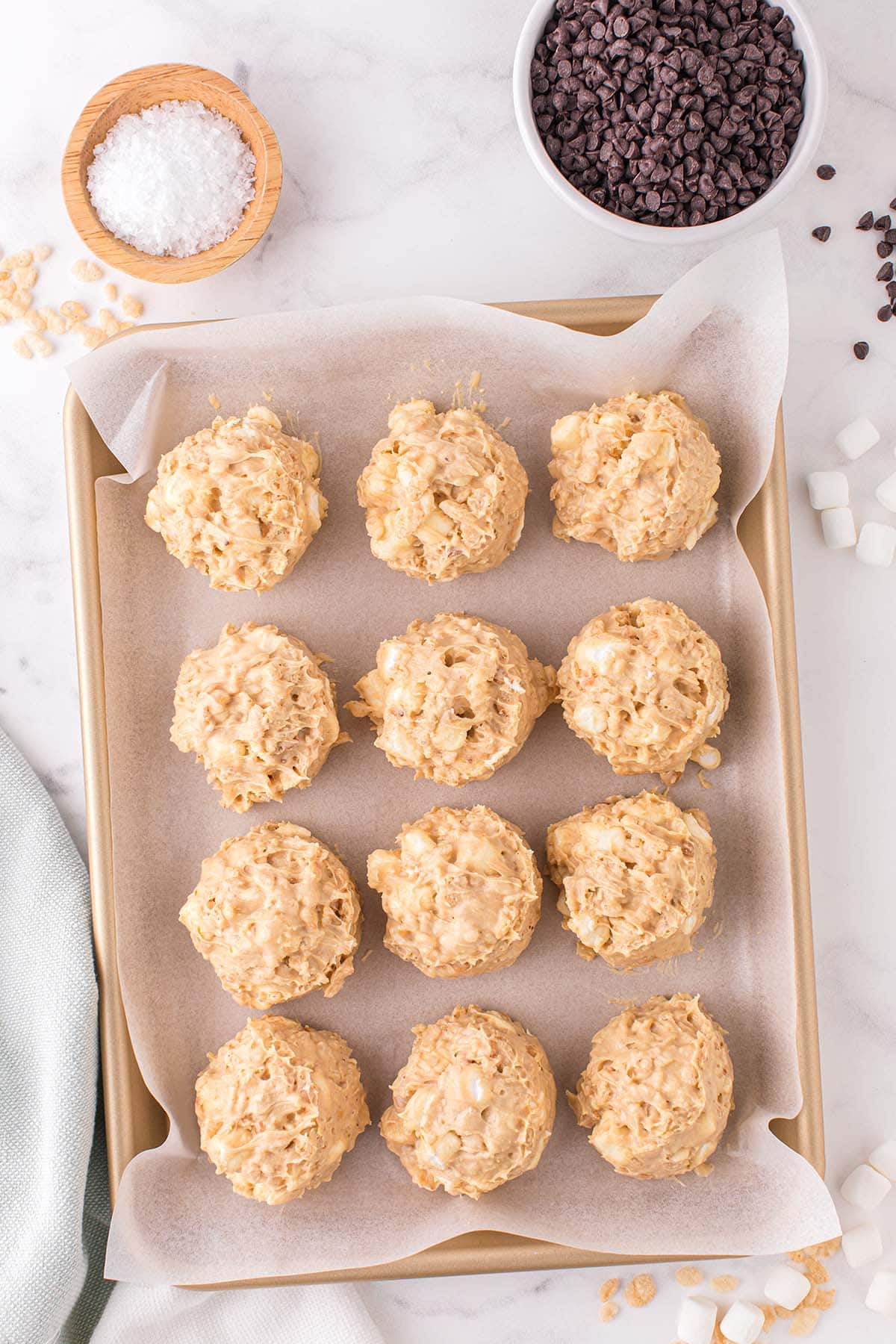Twelve avalanche cookie mounds on a parchment-lined baking sheet before adding toppings.