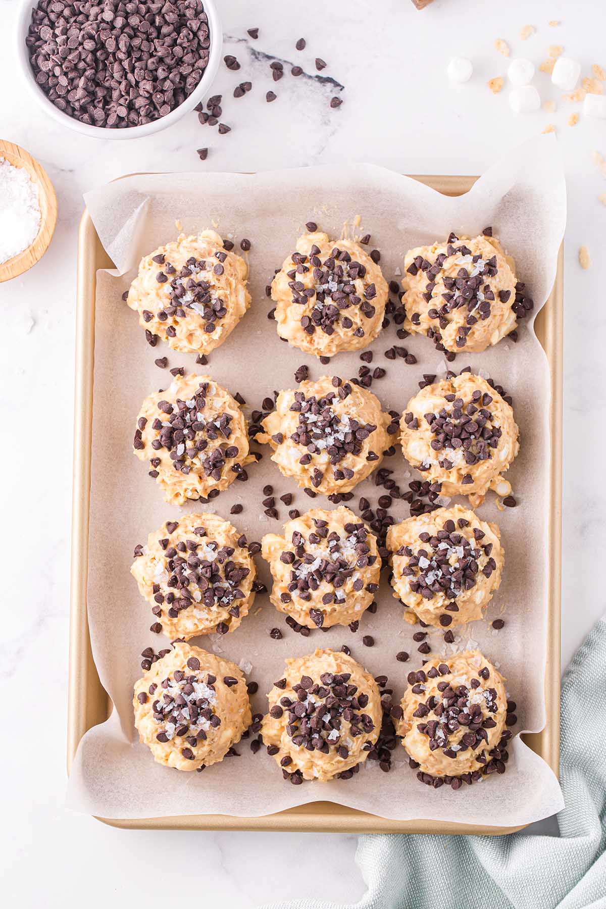 Twelve avalanche cookies topped with mini chocolate chips and flaky sea salt on a parchment-lined baking sheet.