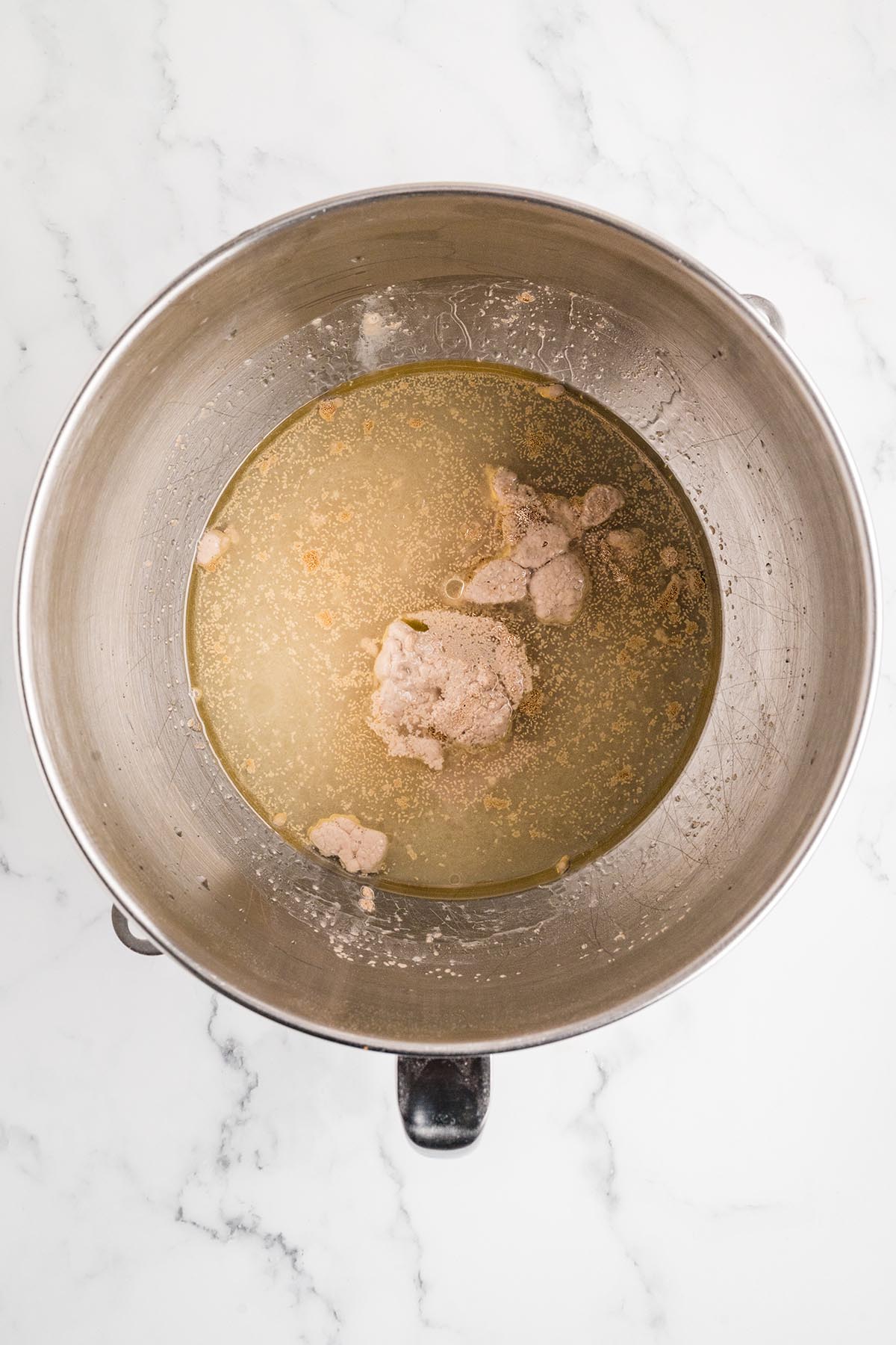 Active yeast blooming in warm water in a stand mixer bowl.