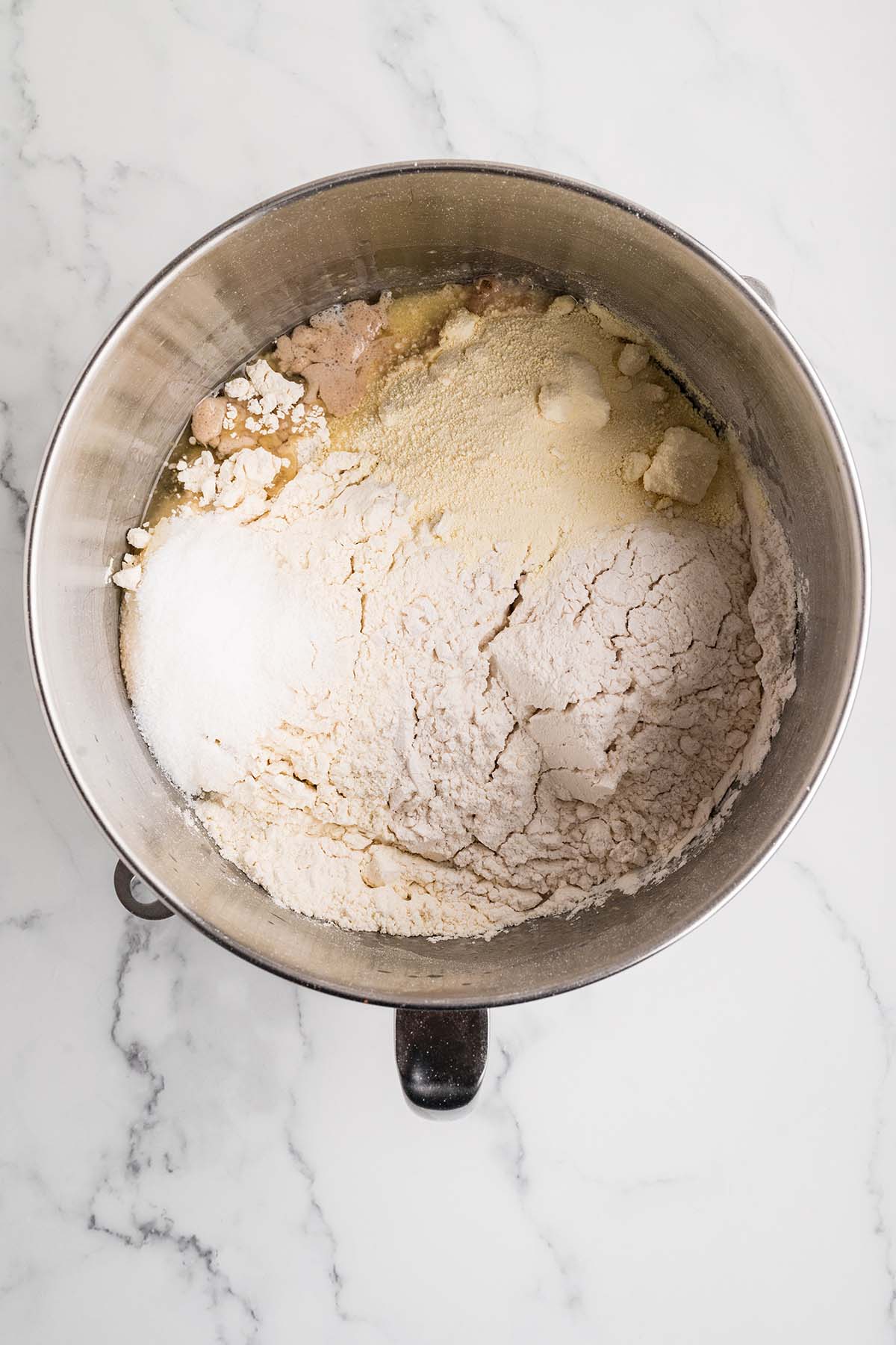 Flour, sugar, and dry ingredients added to yeast mixture in a stand mixer bowl.