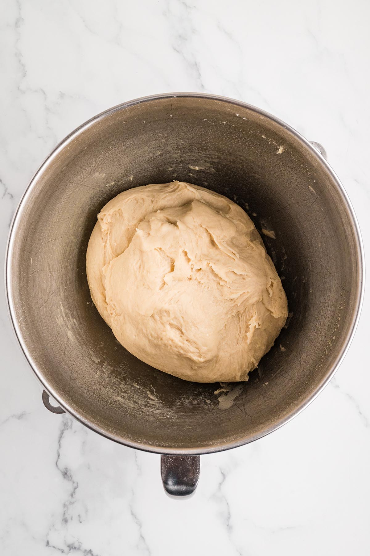 Smooth ball of kneaded roll dough in a stand mixer bowl before rising.