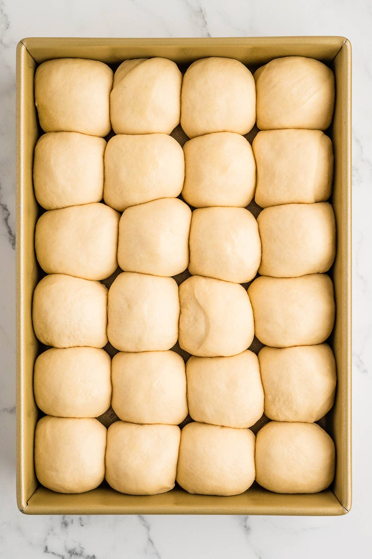 Proofed cafeteria roll dough balls puffed and touching in a gold baking pan, ready to bake.
